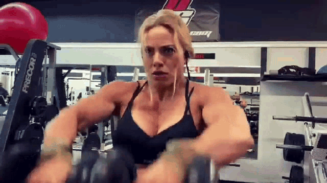 a woman is lifting dumbbells in a gym with a machine that says precor on it