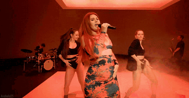 a woman is singing into a microphone while a group of dancers are behind her