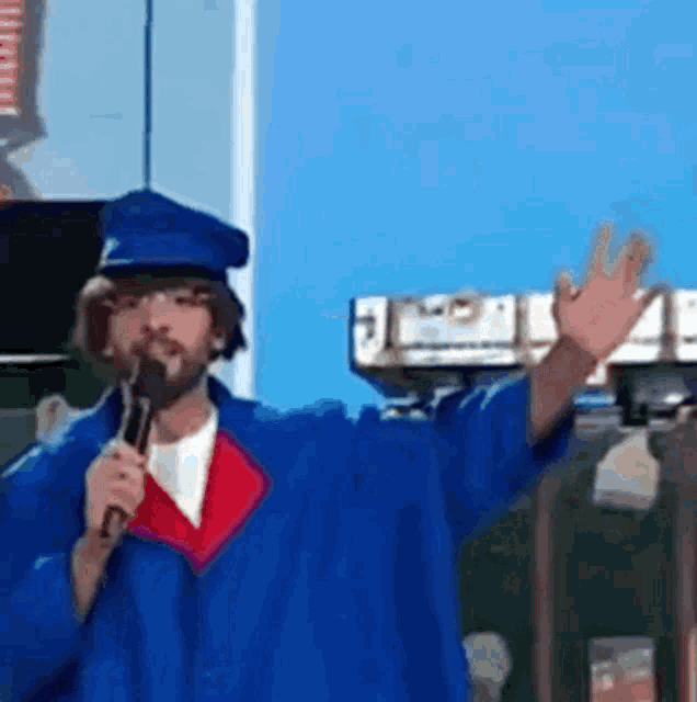 a man in a blue cap and gown is holding a microphone .