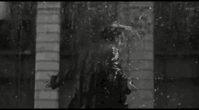 it is a black and white photo of a person standing in the rain .