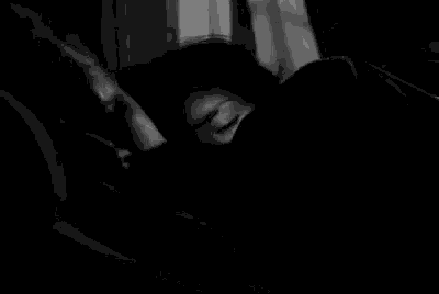 a black and white photo of a person sleeping in a bed with a blanket .