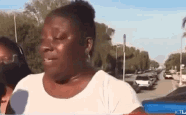 a woman in a white shirt is talking into a microphone while standing on a city street .