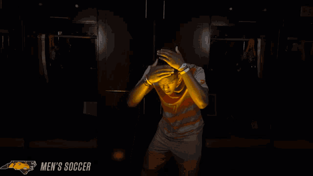 a man stands in a dark room with the words men 's soccer on the bottom right