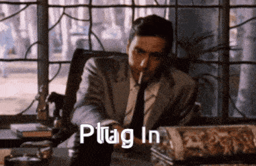 a man in a suit and tie is smoking a cigarette and the words plug in are displayed above him
