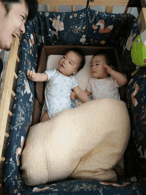 two babies are laying in a crib and one is wearing a fox shirt