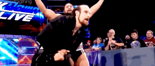 two men are wrestling in front of a crowd at a wrestling match .