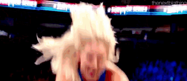 a woman in a wig is dancing in front of a crowd in a stadium .
