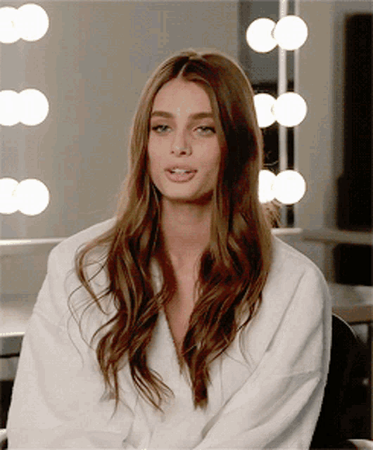 a woman with long brown hair wearing a white robe is sitting in front of a mirror