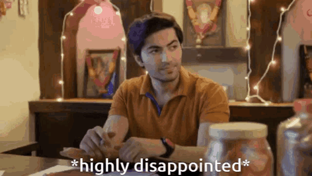 a man is sitting at a table with the words `` highly disappointed '' written on the screen behind him .