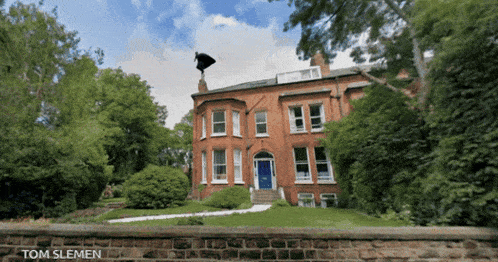 a large red brick house with a blue door is surrounded by trees and bushes with the name tom slemen below it