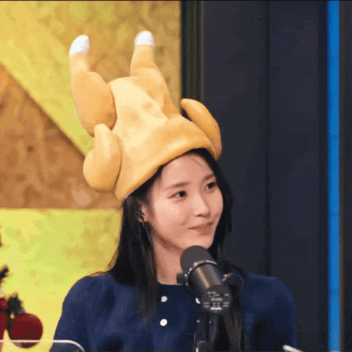 a woman wearing a stuffed chicken hat is smiling in front of a microphone