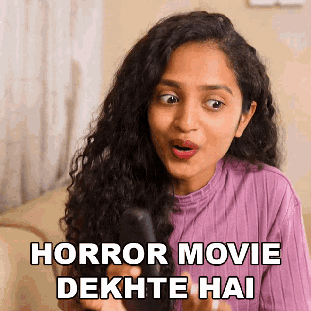 a woman with a surprised look on her face holds a remote control and says horror movie dekhte hai