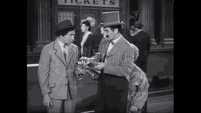 a man in a top hat is talking to another man in a suit in front of a sign that says tickets .