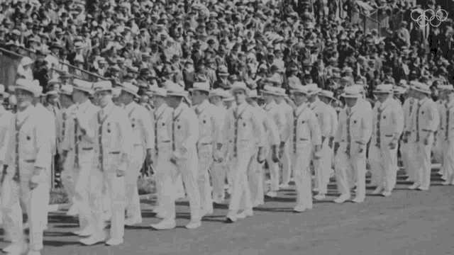 a black and white photo of a parade with the olympic rings in the background