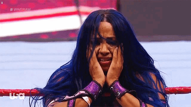 a woman with blue hair is sitting in a wrestling ring covering her face .