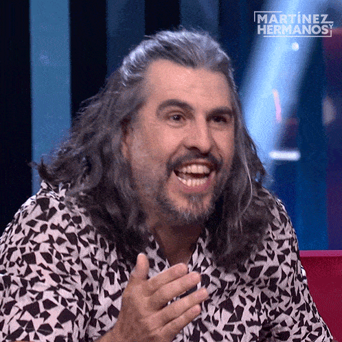 a man with long hair is smiling in front of a martinez hermanos logo