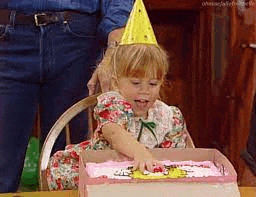 a little girl wearing a party hat is sitting at a table eating a birthday cake .