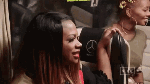 two women are sitting in a mercedes bus and one of them has a flower in her hair .
