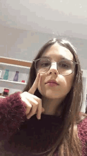 a young woman wearing glasses is taking a selfie in a room .