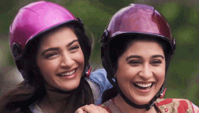 two women wearing pink helmets are smiling and hugging