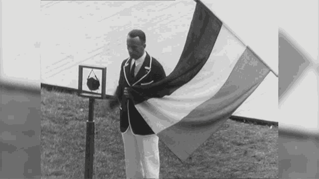 a black and white photo of a man holding a flag in front of a sign that says olympics