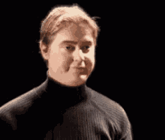 a man in a black turtleneck sweater is making a funny face in the dark .