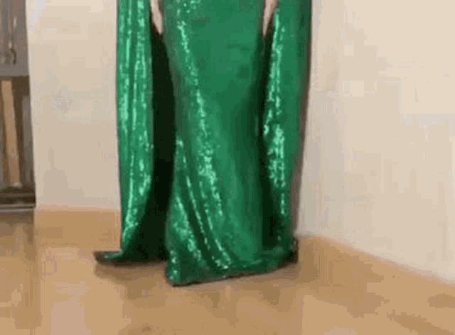 a woman is wearing a long green sequined dress and standing on a wooden floor .