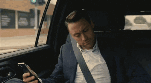 a man in a suit is sitting in a car looking at his phone
