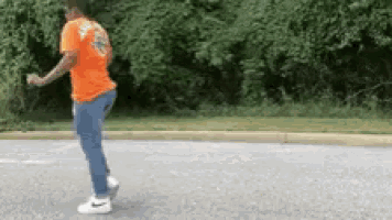 a man in an orange shirt is walking down a road