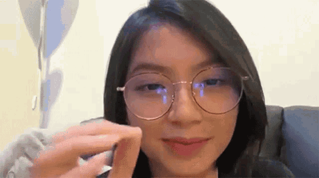 a woman wearing glasses is sitting on a couch holding something in her hand .