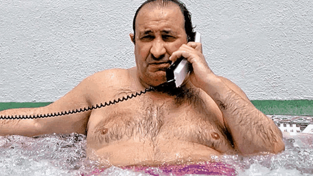 a shirtless man is talking on a phone while sitting in a hot tub