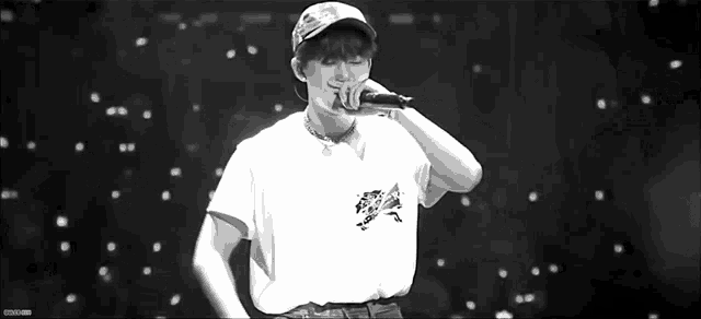 a young man is singing into a microphone while wearing a hat .