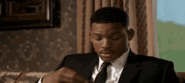 a man in a suit and tie is sitting on a couch looking at his watch .
