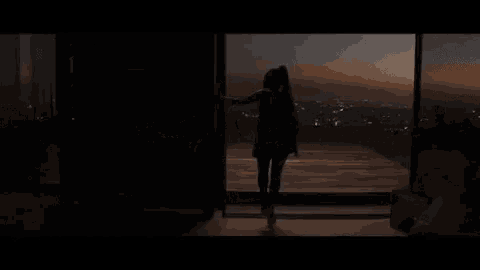 a woman is standing on a balcony overlooking a city at night .