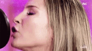 a woman is singing into a microphone with a purple background .