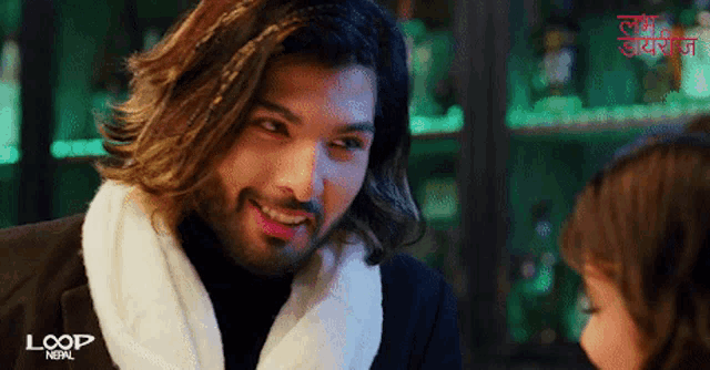 a man with long hair is smiling in front of a sign that says loop nepal on it