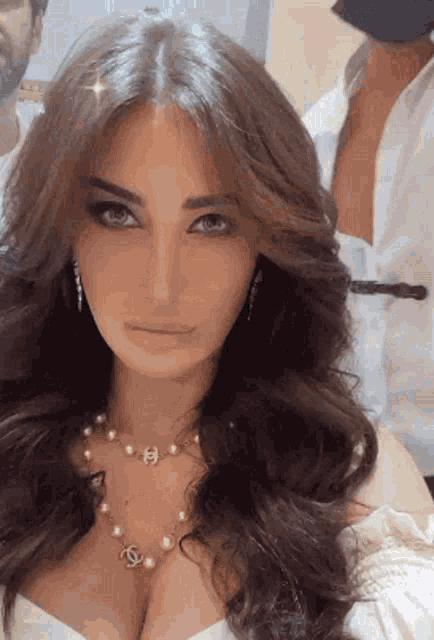 a woman wearing a pearl necklace and earrings looks at the camera .