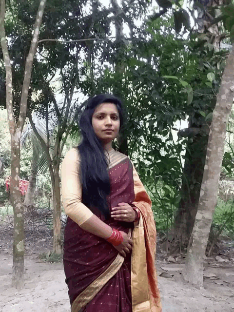 a woman in a red and gold sari stands in a forest