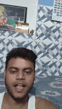 a man in a white tank top stands in front of a wall that has a calendar on it