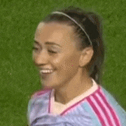 a woman in a pink and blue soccer uniform is smiling on a soccer field .