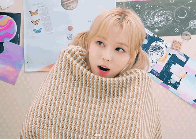 a girl with blonde hair is wrapped in a striped sweater and smiling