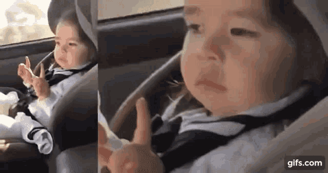 a baby is sitting in a car seat and giving a thumbs up sign .