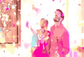 a man and a woman are standing next to each other in a room with confetti falling around them .