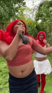 a man in a red wig is singing into a microphone while standing next to another man in a white dress .