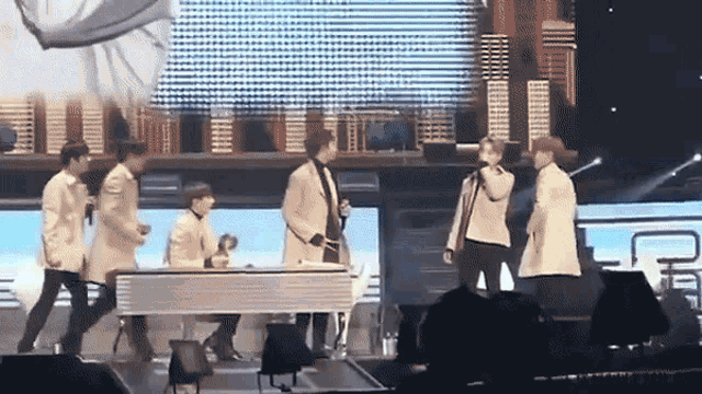 a group of men are standing on a stage with a piano and a microphone