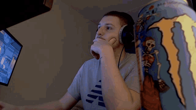 a man wearing headphones is playing a video game next to a monster energy drink