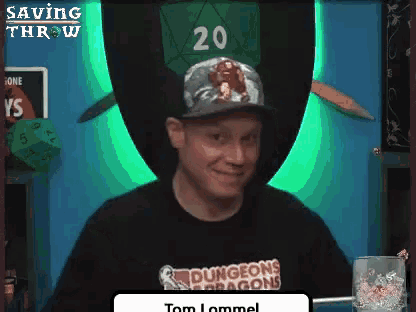 a man wearing a dungeons and dragons hat is smiling in front of a green wall .