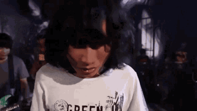 a person with long hair is wearing a white shirt that says green on it .