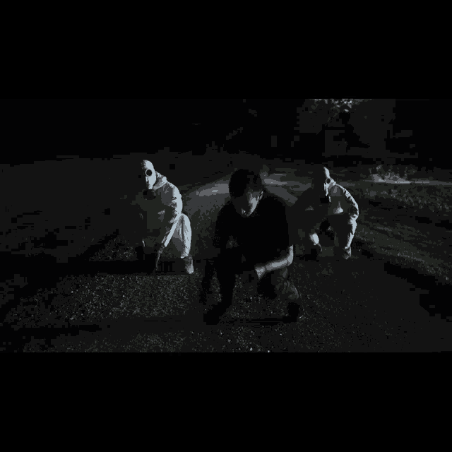 a man in a black shirt is kneeling down in front of two men in white suits