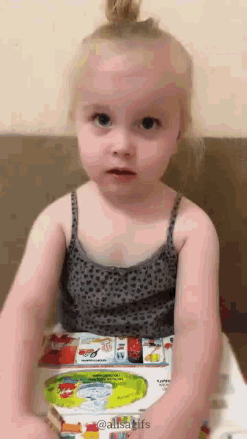 a little girl is sitting on a toilet with a book in her hand .